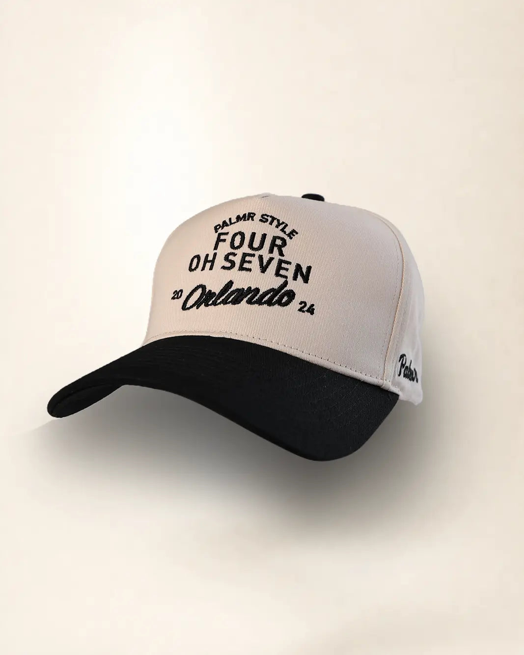 A black and off-white trucker cap with embroidered text reading 'PALMR STYLE FOUR OH SEVEN Orlando 24' on the front panel, shown against a plain light beige background.