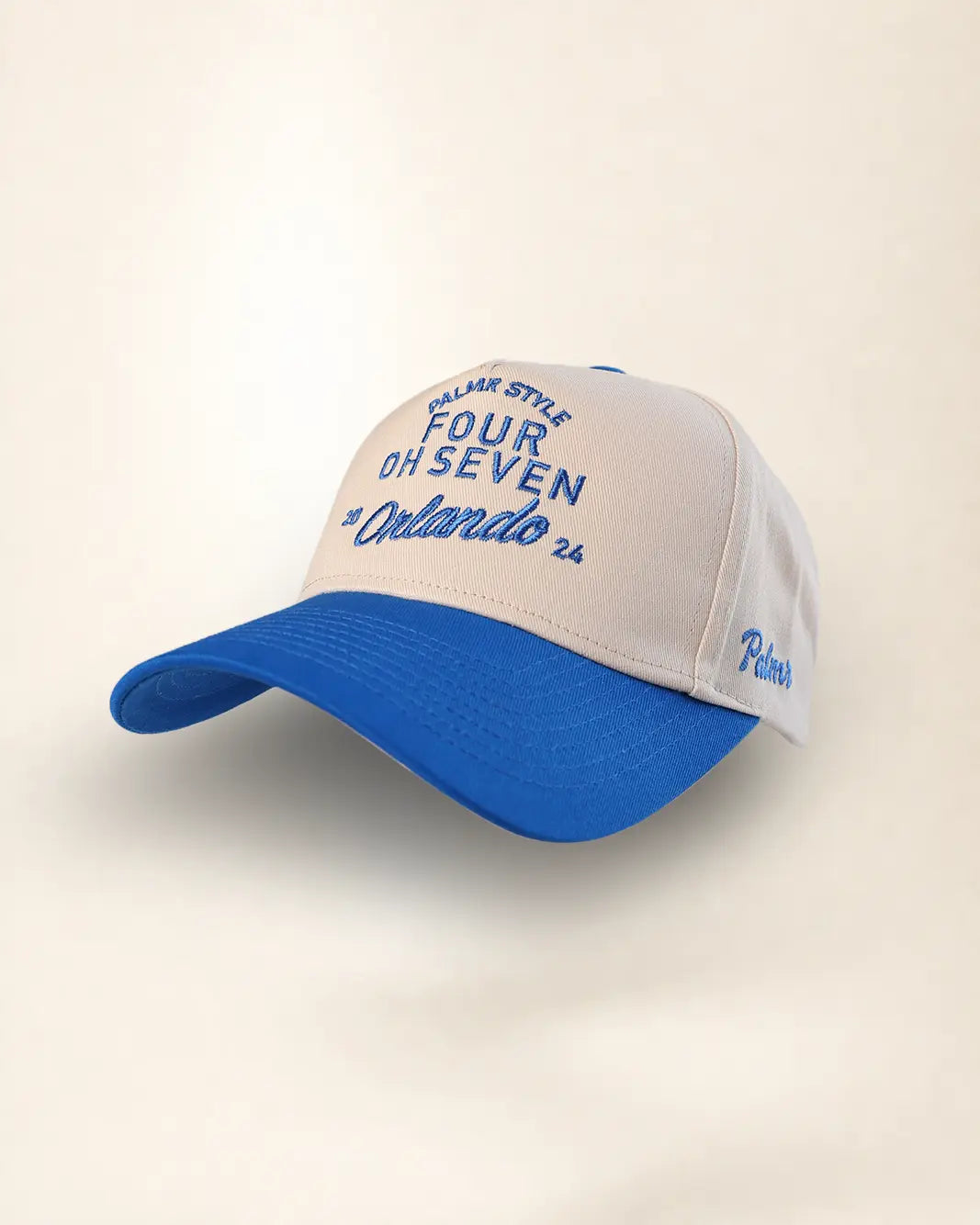 A two-tone baseball cap with a cream-colored front and blue brim, featuring blue embroidered text that reads 'CIVIL AIR STYLE FOUR OH SEVEN #Orlando 26' on the front panel.
