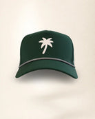 A dark green baseball cap featuring a white palm tree logo on the front and a silver chain detail along the brim, set against a plain light beige background.