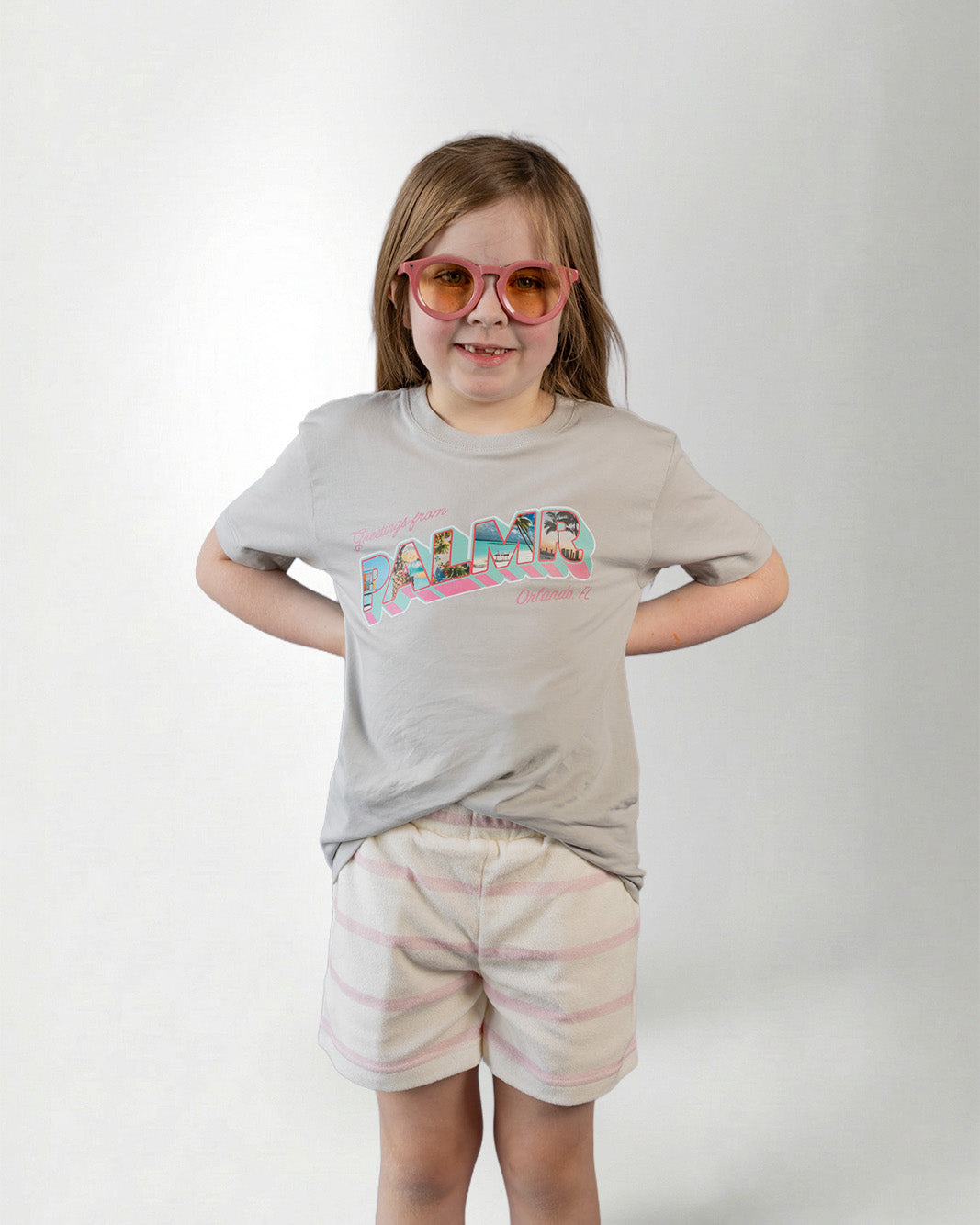 Person wearing a light gray t-shirt with colorful text, striped shorts on a plain background.