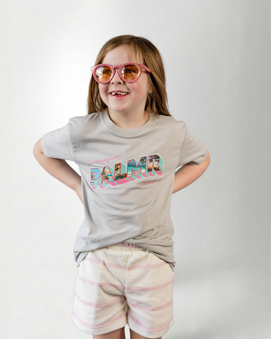 Person wearing a light gray t-shirt with colorful text, striped shorts on a plain background.