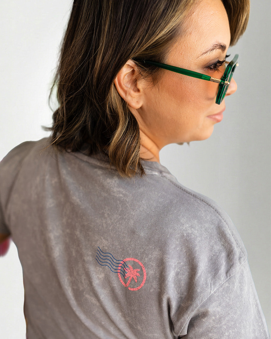 Woman wearing a gray t-shirt with colorful text and blue jeans, posing against a plain background.