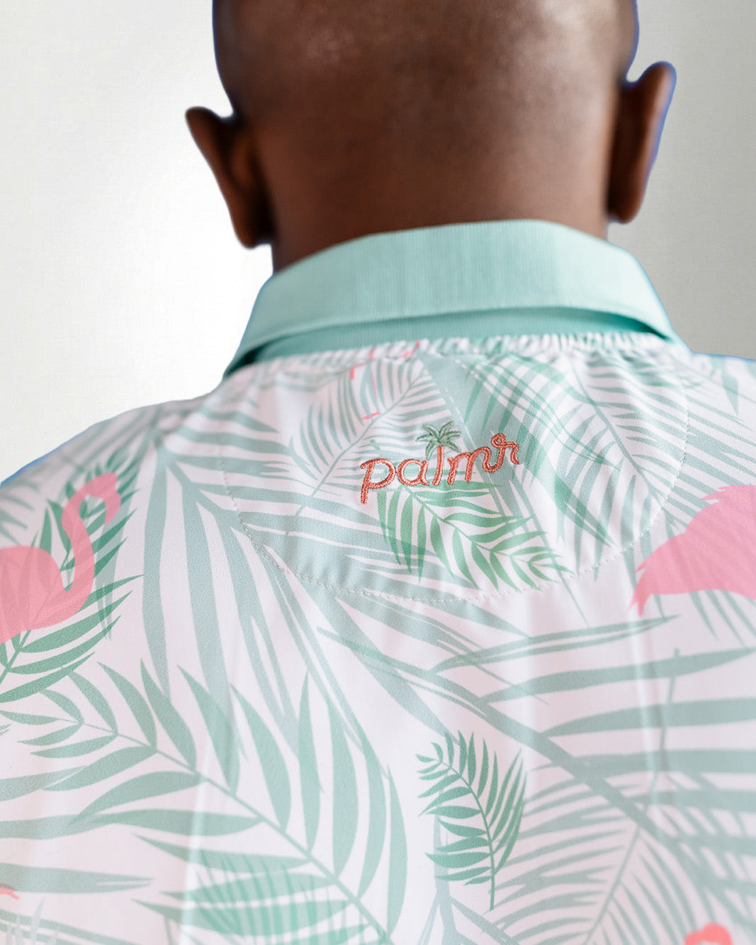 Person wearing a shirt with palm tree and flamingo pattern, brand 'palms' visible.