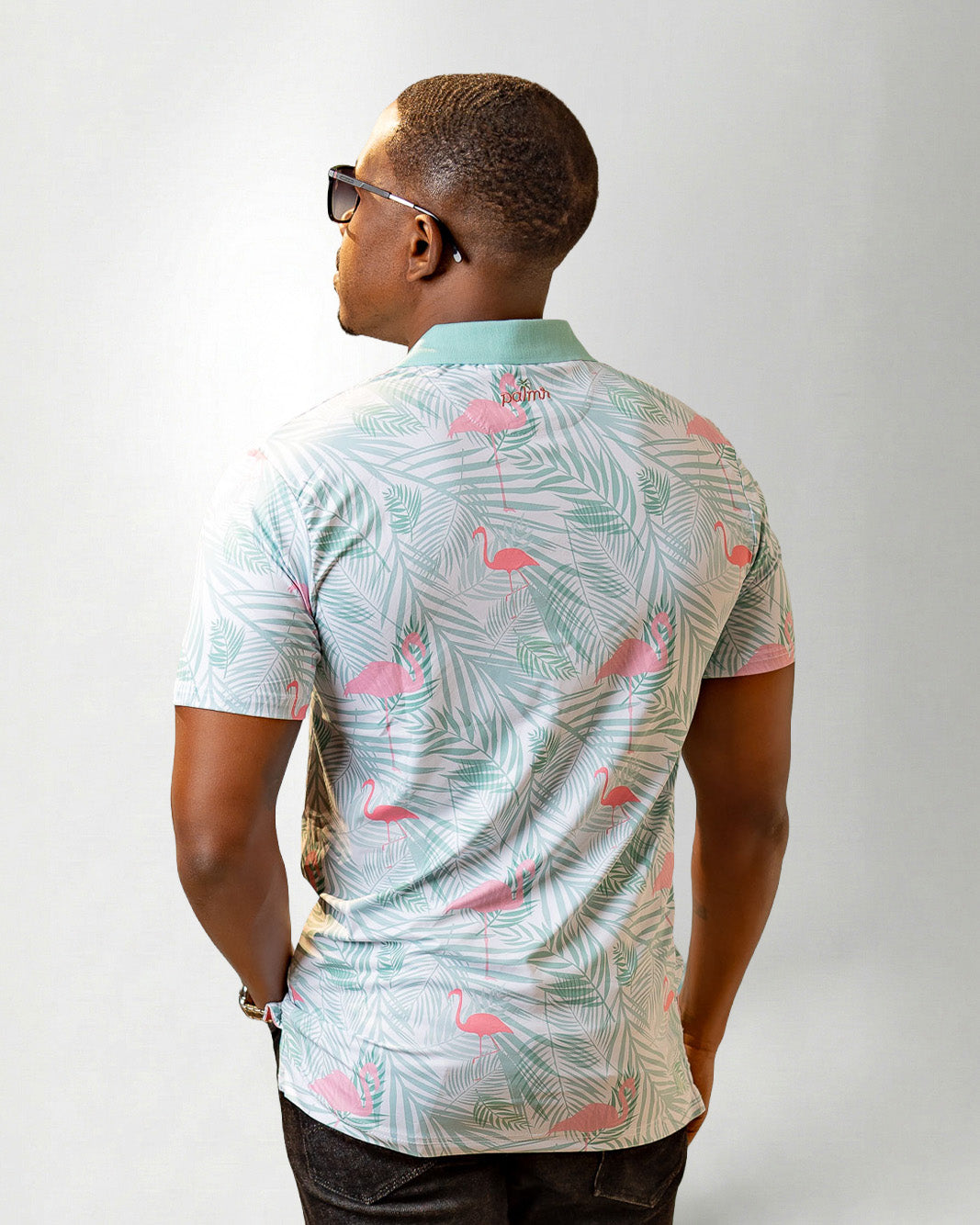Man wearing a patterned shirt with flamingo and leaf design on a plain background
