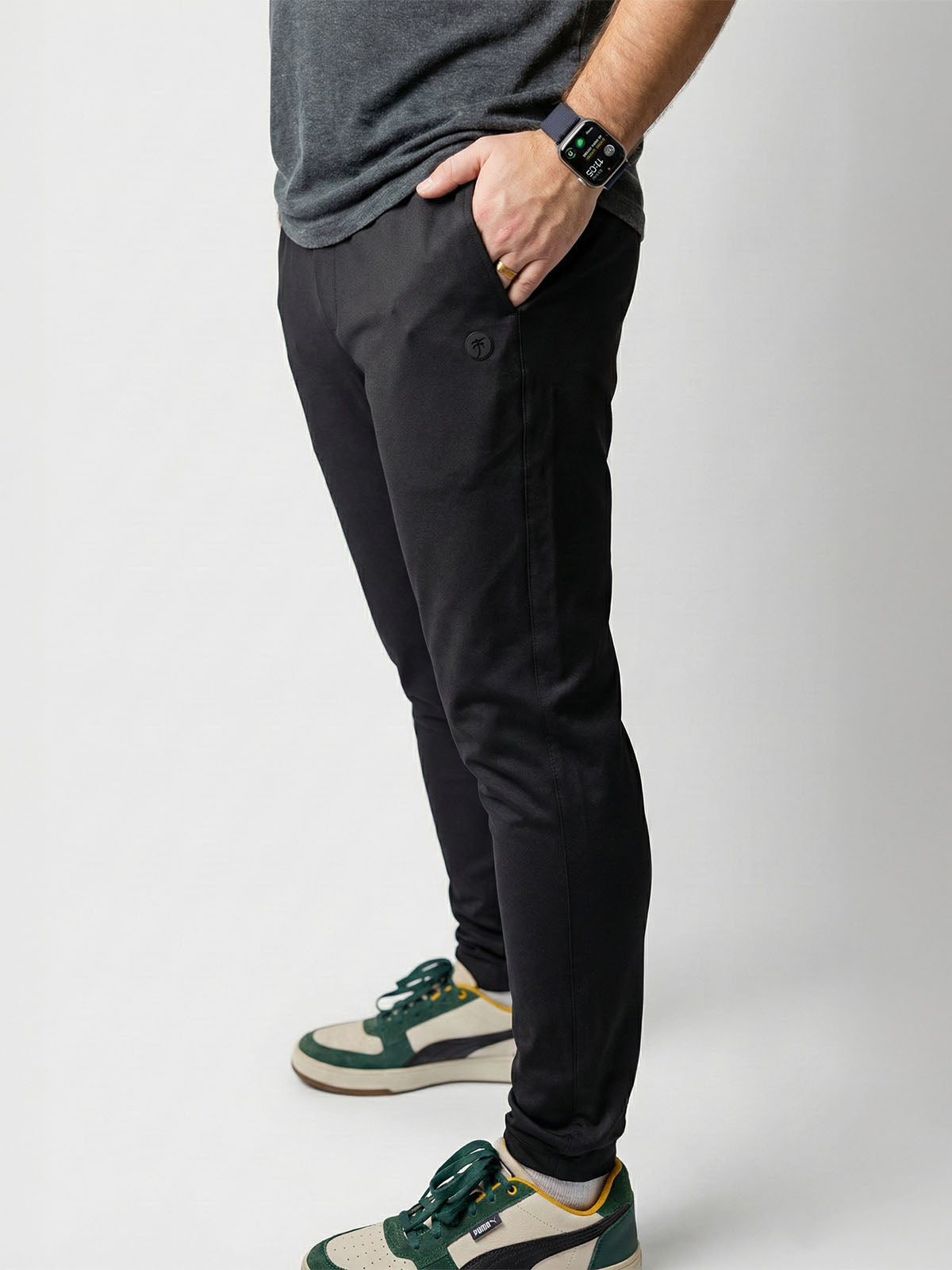 Person wearing black pants and green sneakers on a plain background