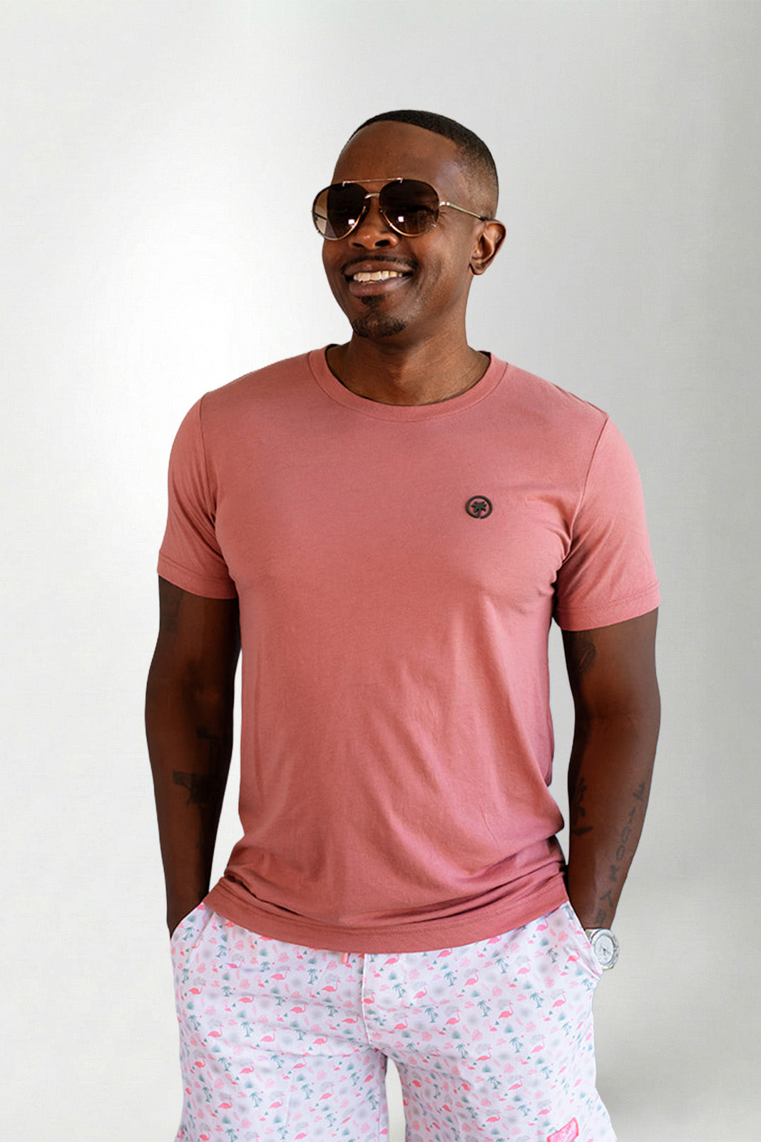 Man wearing a pink t-shirt and light-colored pants with a subtle pattern on a plain background
