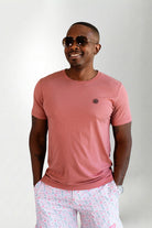 Man wearing a pink t-shirt and light-colored pants with a subtle pattern on a plain background