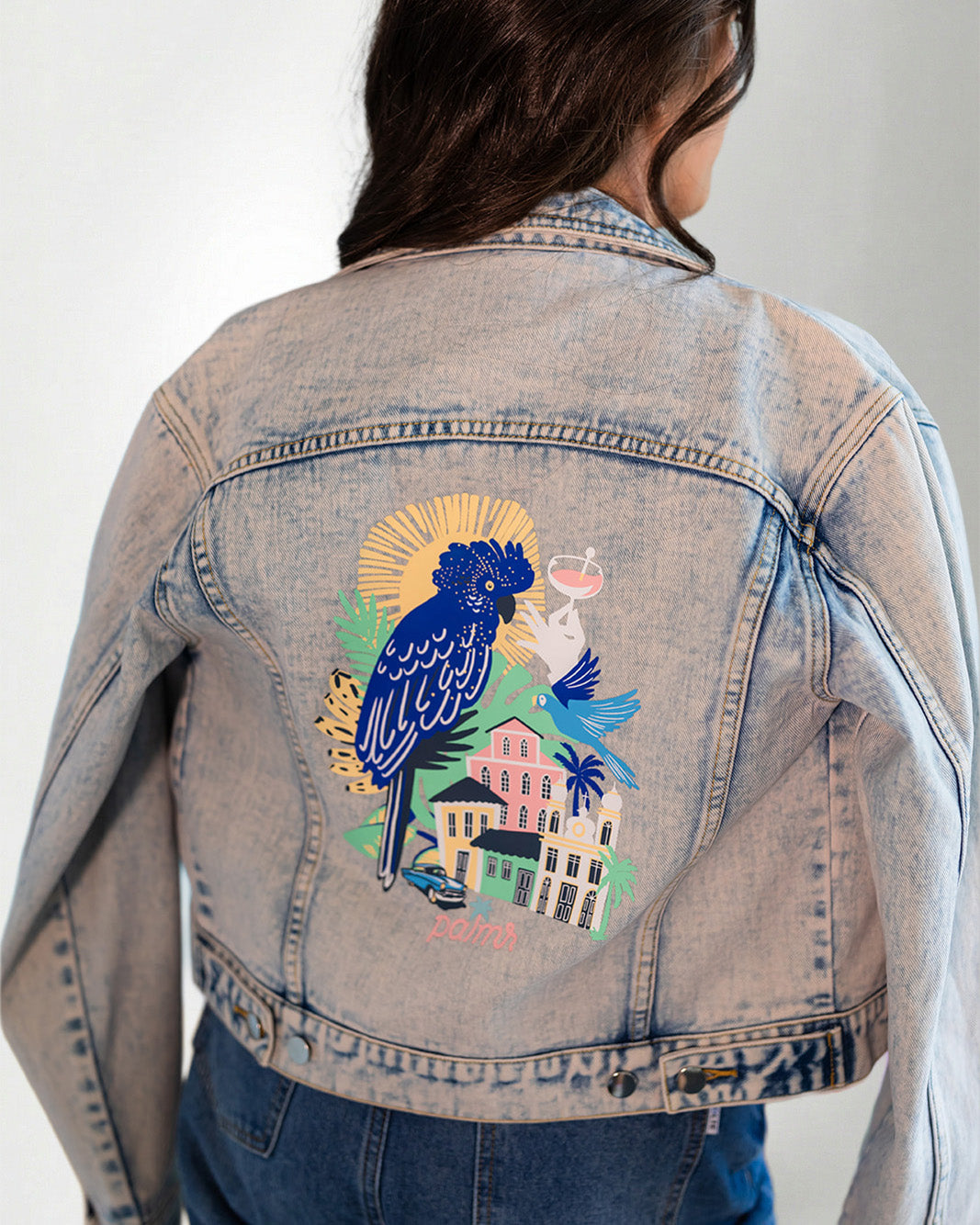 Denim jacket with a colorful parrot design on the back, worn by a person.