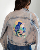Denim jacket with a colorful parrot design on the back, worn by a person.