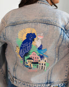 Denim jacket with a colorful parrot design on the back, worn by a person.