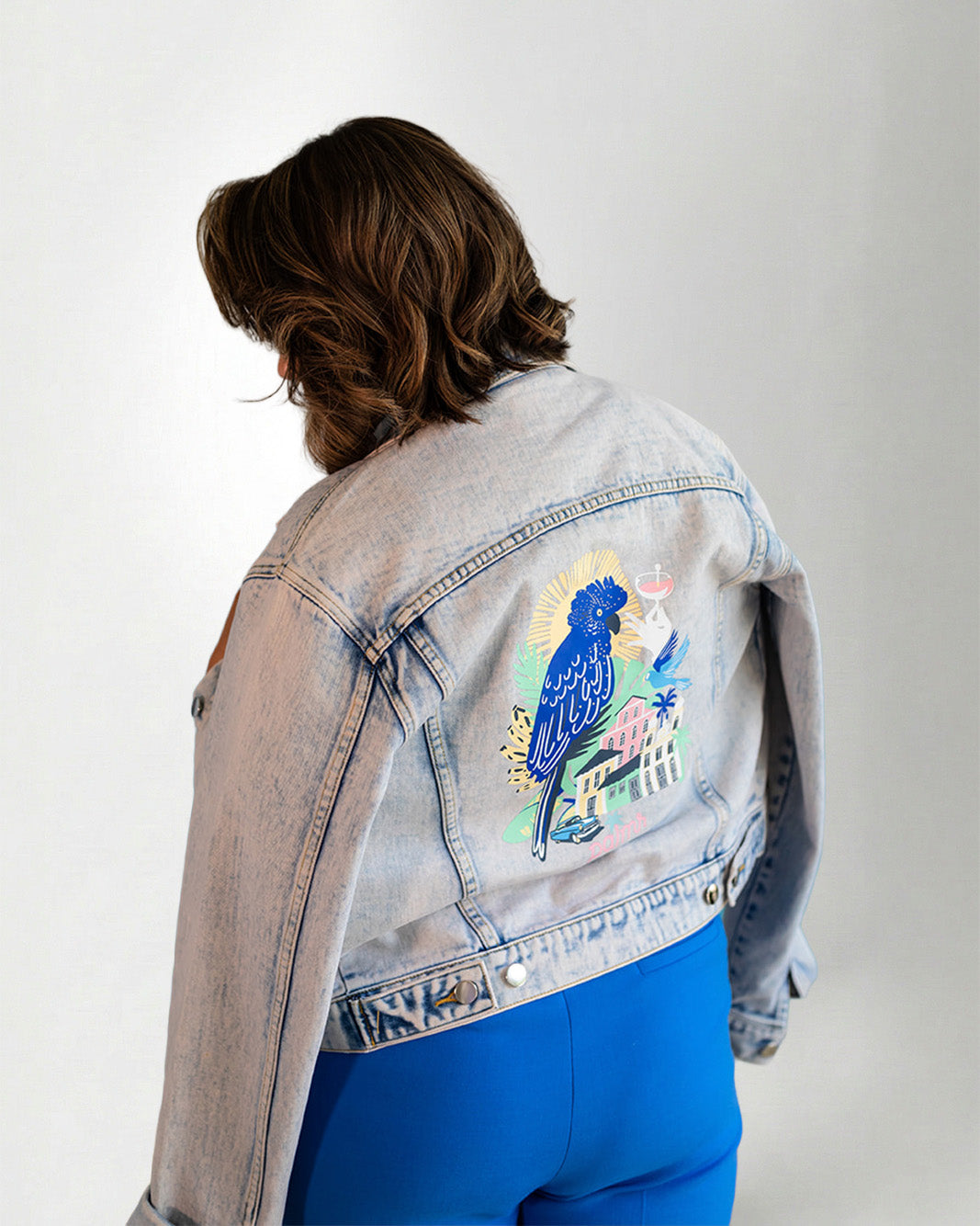 Denim jacket with a colorful parrot design on the back, worn by a person.