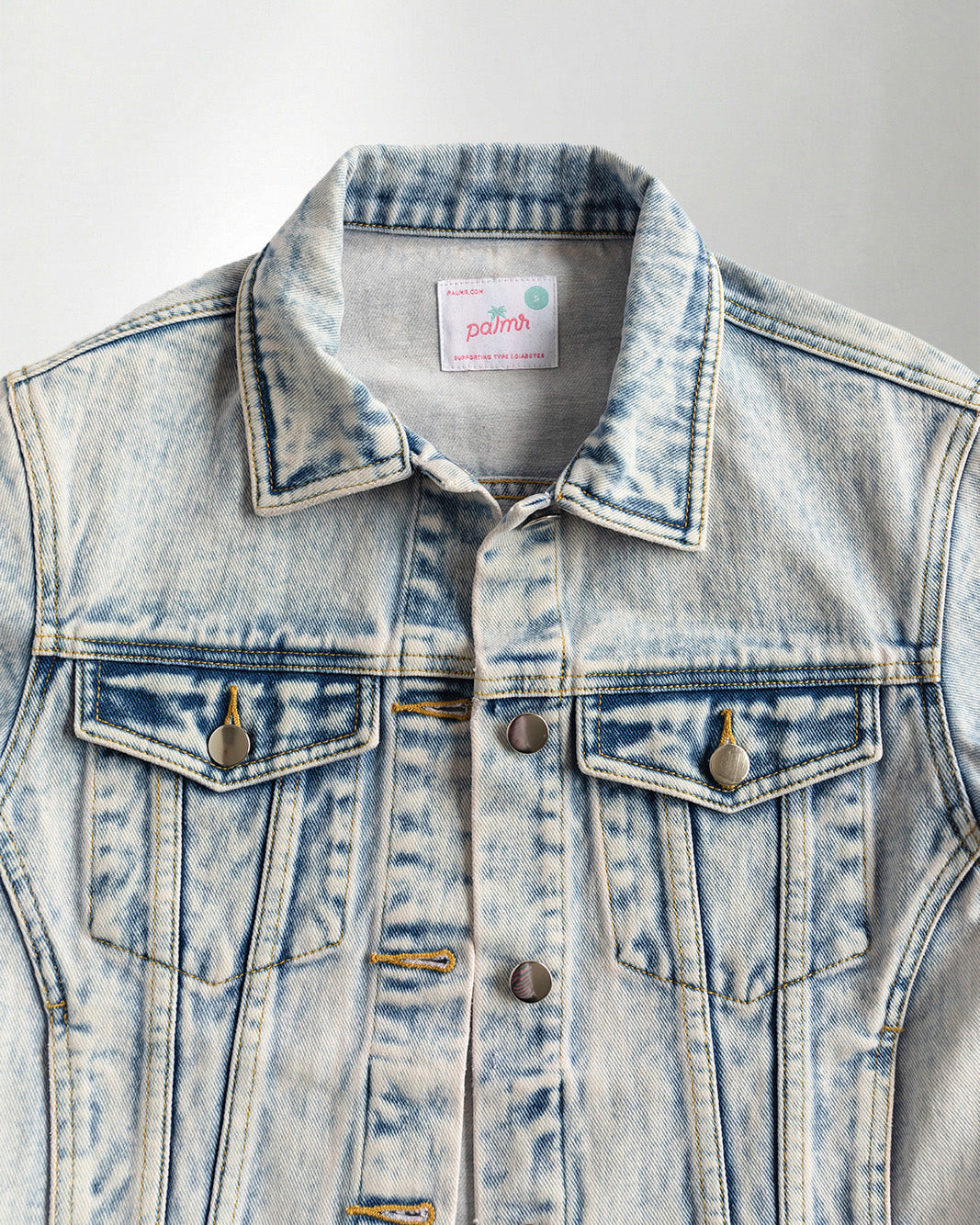 Denim jacket with a colorful parrot design on the back, worn by a person.