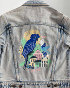 Denim jacket with a colorful parrot design on the back, worn by a person.