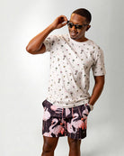 Person wearing a white shirt with a palm tree pattern and black shorts with pink flamingo pattern on a plain background