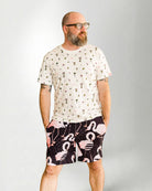 Person wearing a white shirt with a palm tree pattern and black shorts with pink flamingo pattern on a plain background