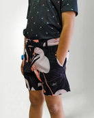 Person wearing a black patterned shirt and shorts with a white bird design on a plain background