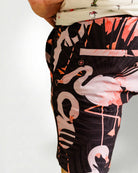 Person wearing a white shirt with a palm tree pattern and black shorts with pink flamingo pattern on a plain background