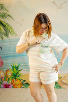 Person wearing a light-colored outfit with a 'Palm' logo, standing in front of a colorful beach mural.