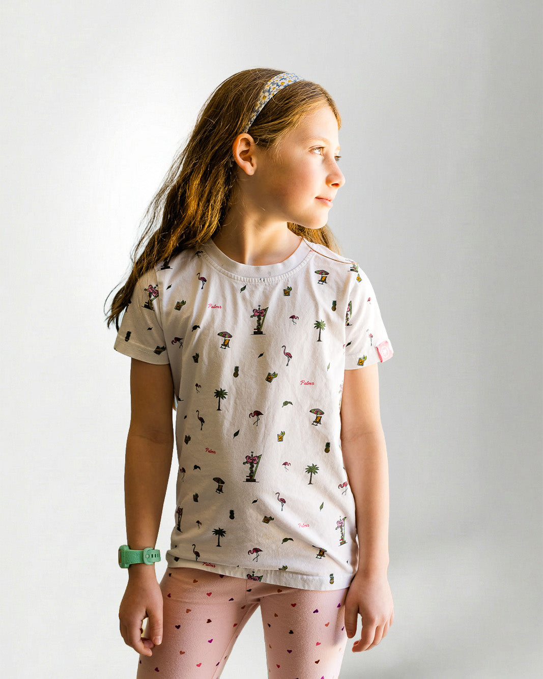 Young girl wearing a patterned shirt and pink pants on a plain background