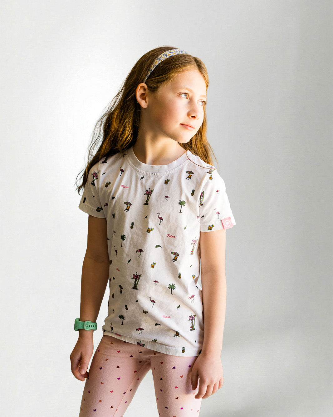Young girl wearing a patterned shirt and pink pants on a plain background