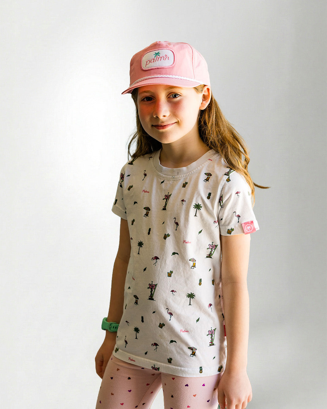 Young girl wearing a patterned shirt and pink pants on a plain background