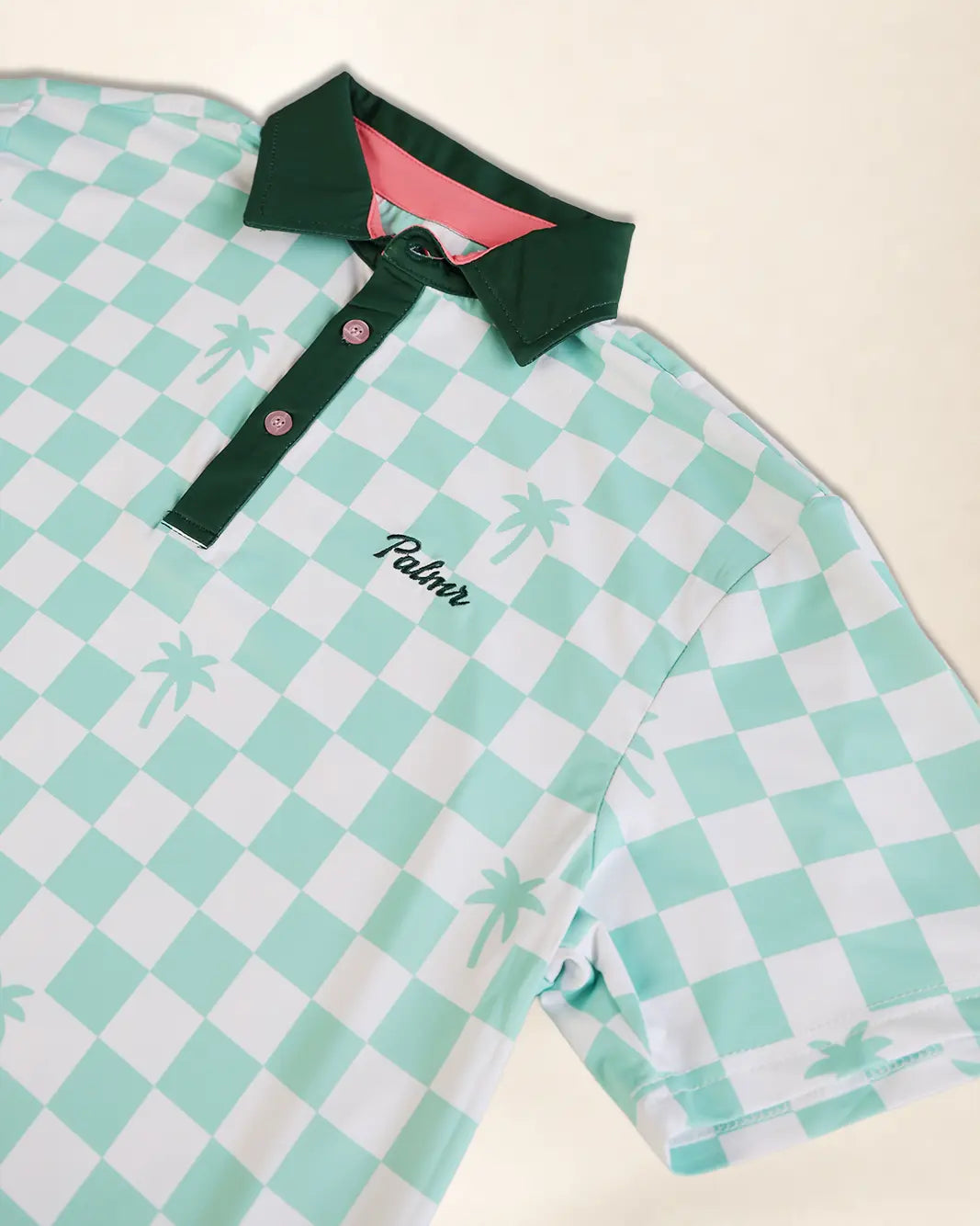A short-sleeve polo shirt with a mint green and white checkered pattern, featuring a solid dark green collar and placket with pink buttons. The word 'Palmr' is embroidered in black script on the chest.