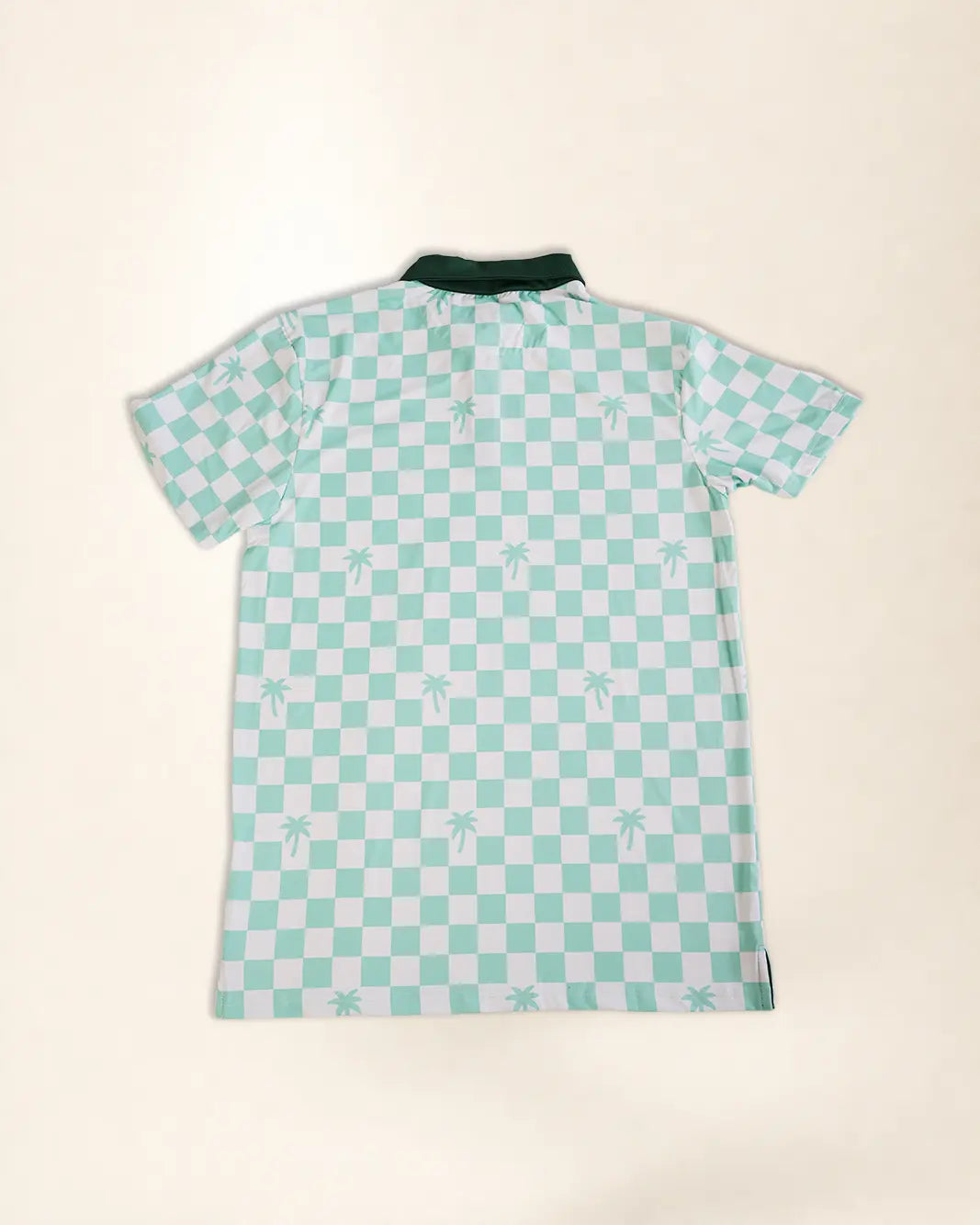 A short-sleeve polo shirt with a mint green and white checkerboard pattern, featuring small palm tree motifs on the squares and a solid dark green collar, laid flat against a light beige background.