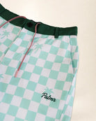 Close-up of a pair of shorts with a mint green and white checkered pattern, featuring a dark green elastic waistband, pink drawstrings, and a small embroidered 'Palmr' logo with a palm tree on the lower left leg.