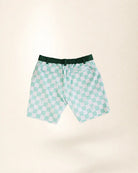 A pair of men's swim trunks featuring a mint green and white checkered pattern with small palm tree motifs, a dark green elastic waistband, and a white drawstring, shown against a solid cream background.