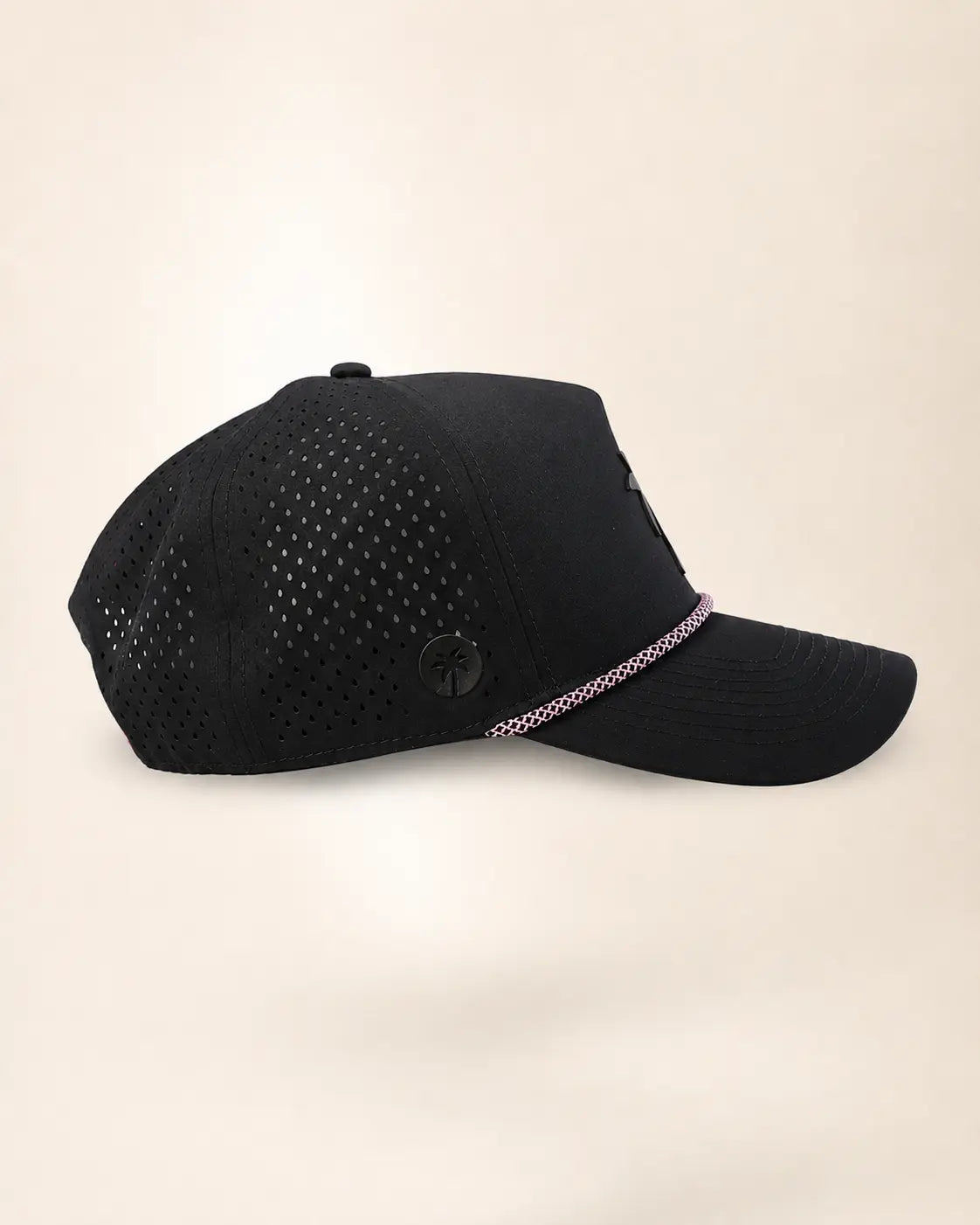 A black baseball cap with perforated side panels and a curved brim, featuring a thin pink and white patterned trim along the edge of the brim, set against a solid light beige background.