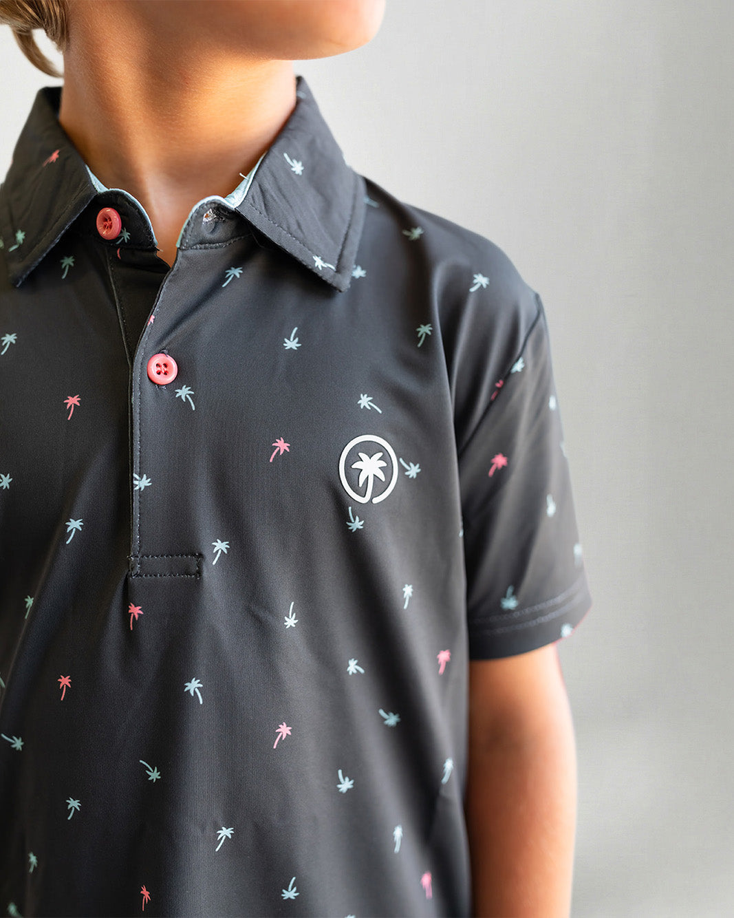 Young boy wearing a dark polo shirt with a pattern on a plain background