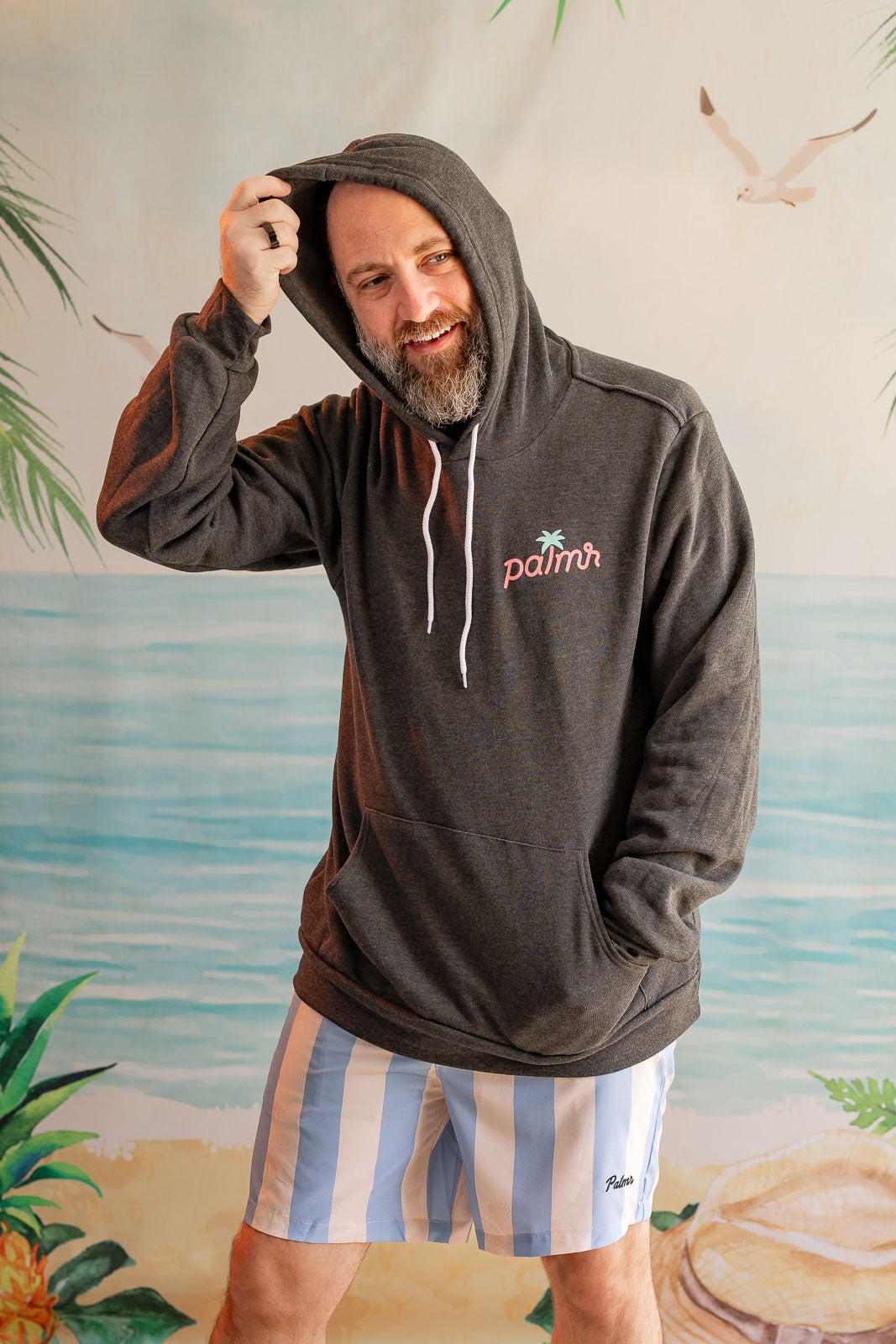Man wearing a hoodie with a palm tree design in front of a beach mural.