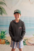 Child wearing a hoodie and cap with a beach mural in the background