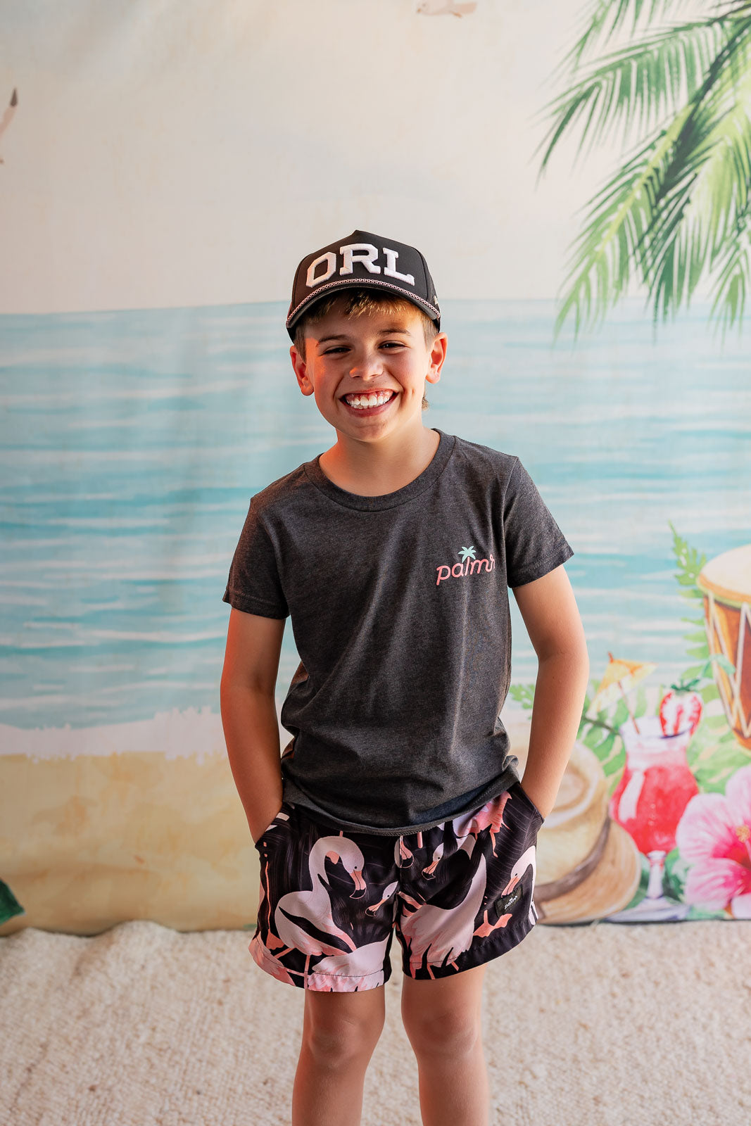 Child wearing a cap and t-shirt with a beach-themed backdrop