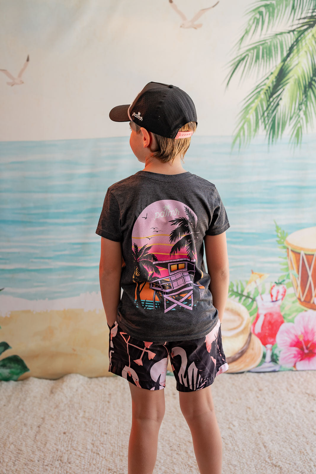 Child wearing a graphic t-shirt and shorts in front of a beach mural.