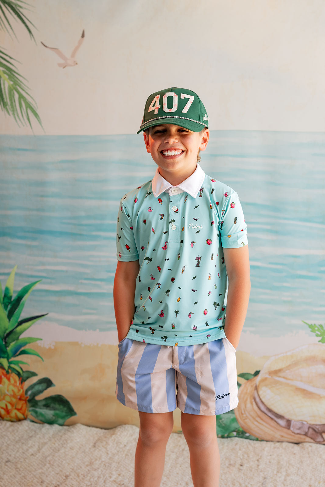 Child wearing a patterned shirt and cap with a beach-themed backdrop