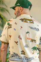 Man wearing a patterned shirt with palm trees, boats, and other designs.