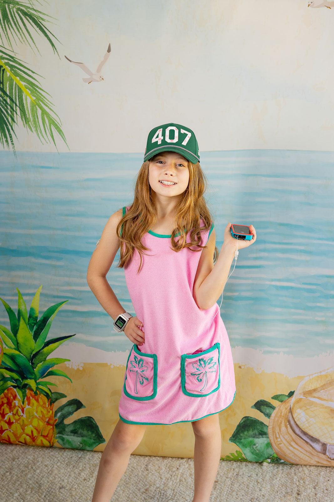 Young girl in a pink dress with green accents standing in front of a beach-themed wall.