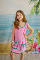 Young girl in a pink dress with green trim standing in front of a beach-themed mural.