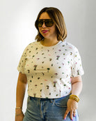 Woman wearing a patterned shirt and jeans with sunglasses on a plain background