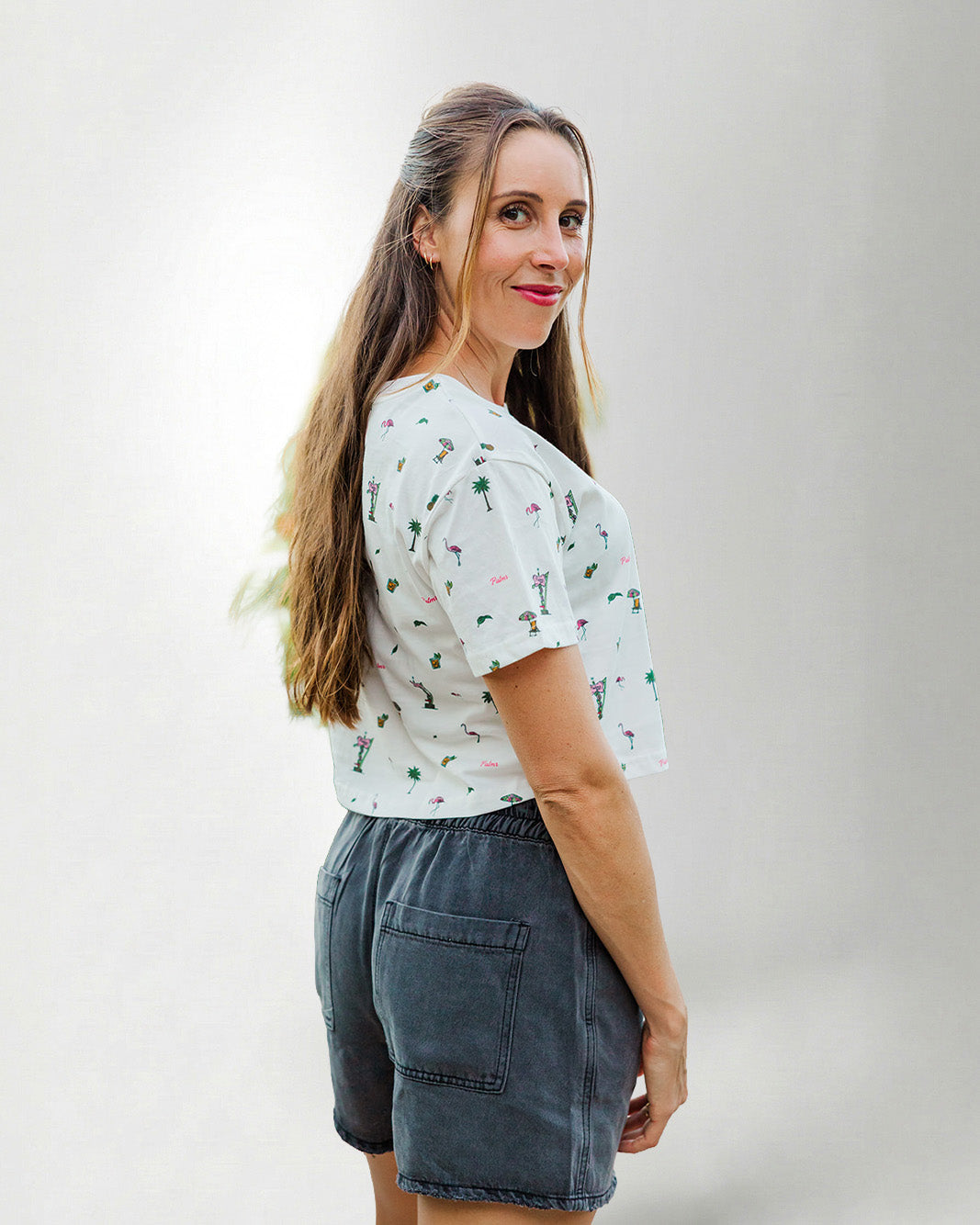 Woman wearing a patterned shirt and jeans with sunglasses on a plain background