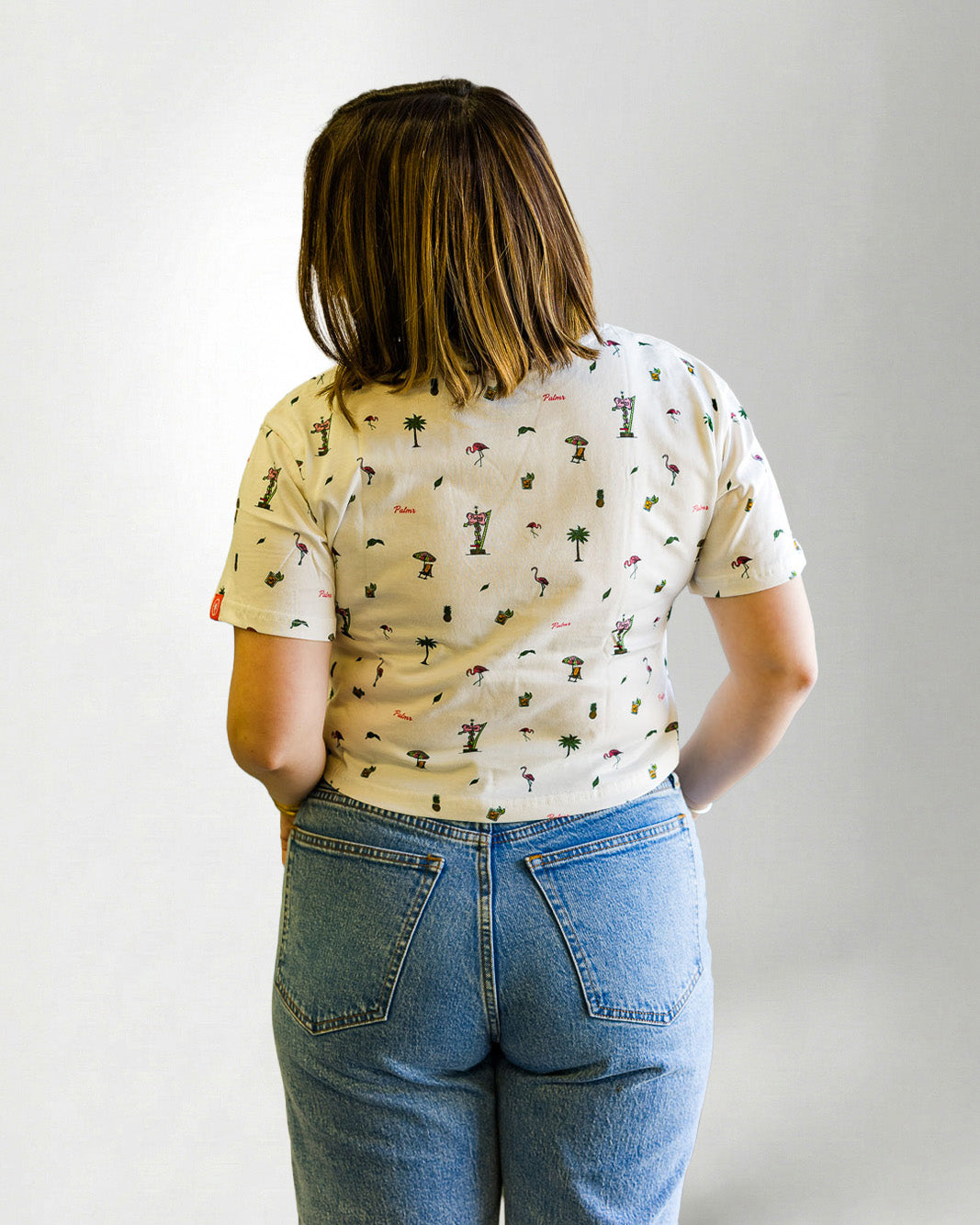 Woman wearing a patterned shirt and jeans with sunglasses on a plain background
