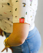 Woman wearing a patterned shirt and jeans with sunglasses on a plain background