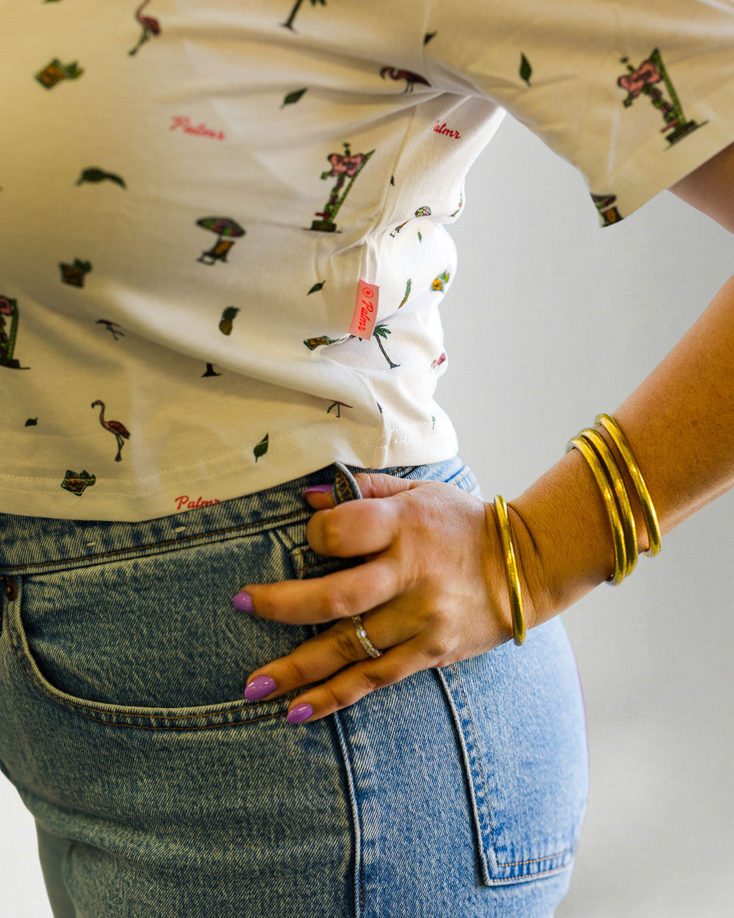 Woman wearing a patterned shirt and jeans with sunglasses on a plain background