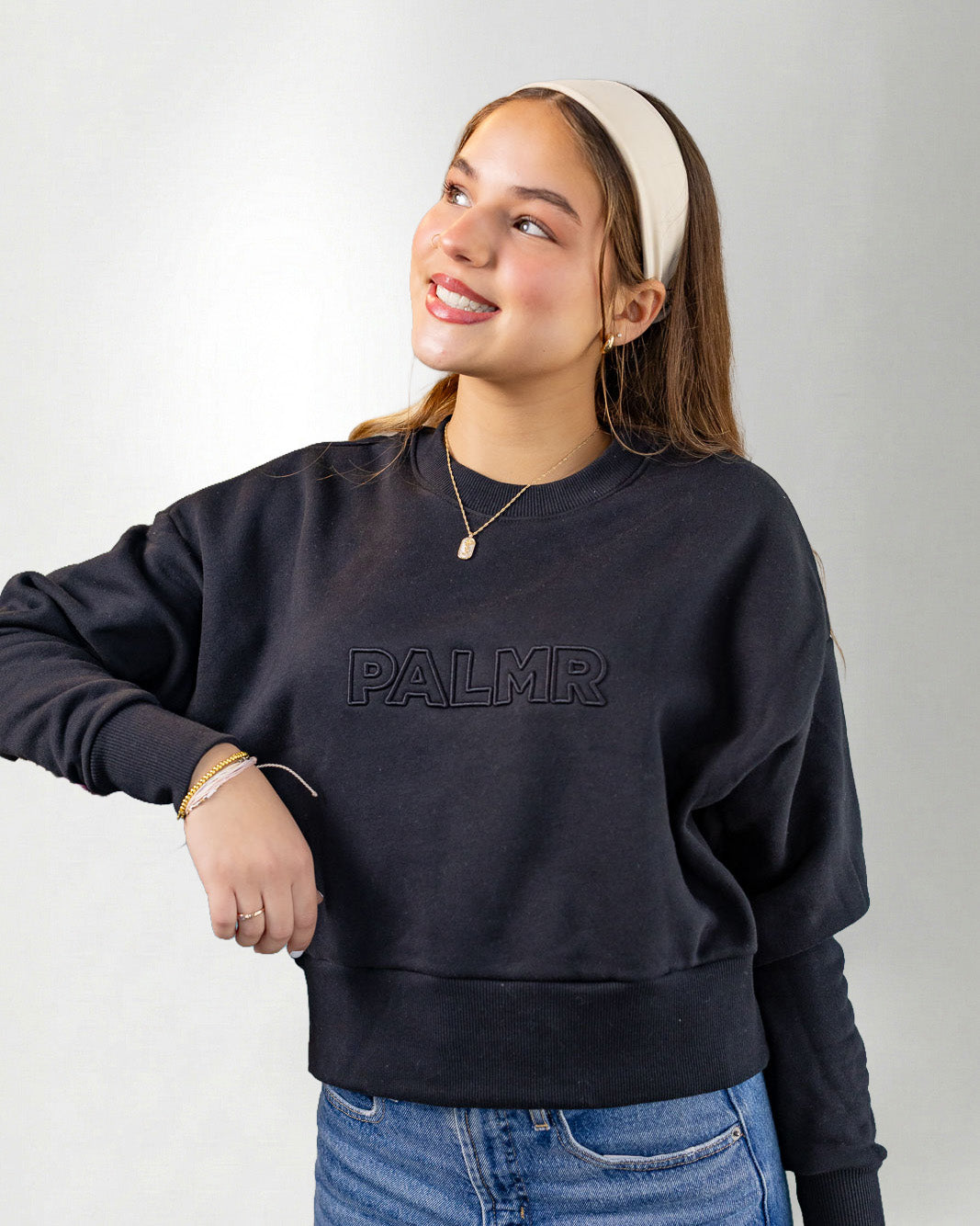 Woman wearing a navy blue sweatshirt with 'PALMR' branding, holding a floral-patterned bag against a white background.