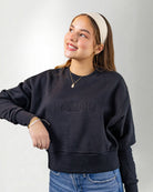Woman wearing a navy blue sweatshirt with 'PALMR' branding, holding a floral-patterned bag against a white background.