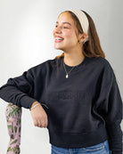 Woman wearing a navy blue sweatshirt with 'PALMR' branding, holding a floral-patterned bag against a white background.