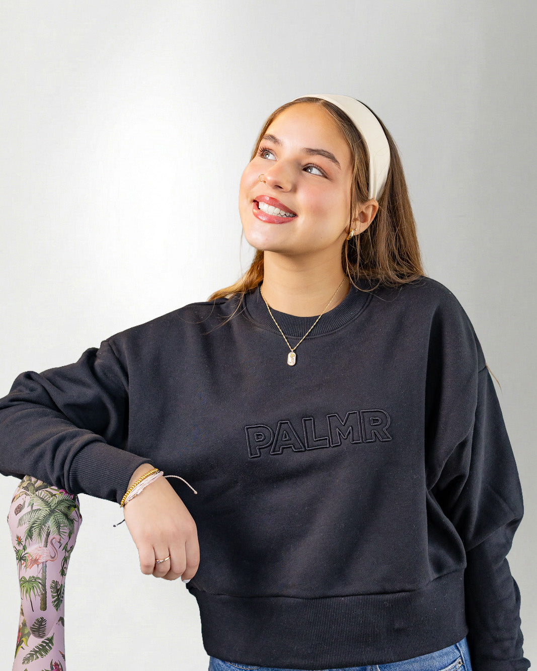 Woman wearing a navy blue sweatshirt with 'PALMR' branding, holding a floral-patterned bag against a white background.