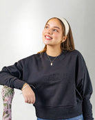 Woman wearing a navy blue sweatshirt with 'PALMR' branding, holding a floral-patterned bag against a white background.