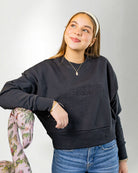 Woman wearing a navy blue sweatshirt with 'PALMR' branding, holding a floral-patterned bag against a white background.
